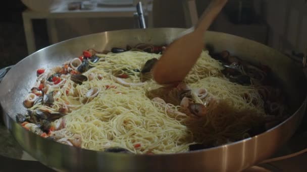 A cook is stirring with long wooden spatula a dish of pasta and seafood. Closeup — Wideo stockowe