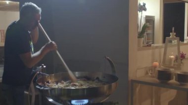 Adam ateşin üzerinde büyük bir tavada makarna ve deniz ürünleri karıştırıyor..