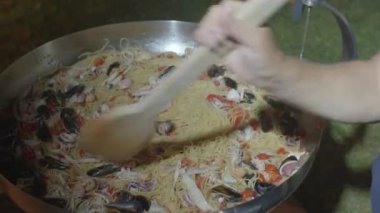 Bir aşçı, uzun ahşap bir spatula, bir tabak makarna ve deniz ürünüyle karıştırıyor. Yakın çekim.
