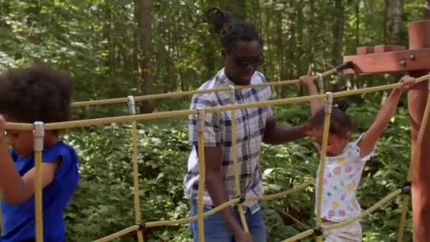 Père avec les enfants joue sur l'aire de jeux forestière, les aide à former leur agilité. — Video