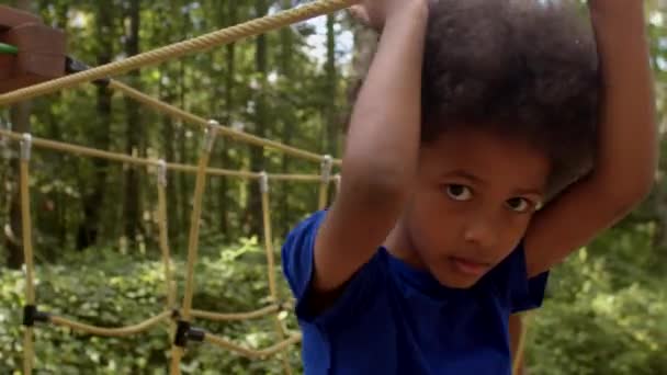 Portrait of an African American boy overcomes a rope obstacle, looks at camera. — Stock video