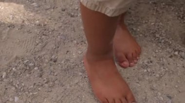 Oyun parkında kumların üzerinde yürüyen çıplak çocuk ayaklarının yakın çekimi..