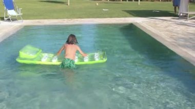 Child uses inflatable mattress while swimming in pool during summer vacations.