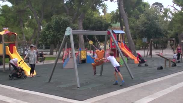 Children play in the city playground, swing on a swing. Kids-friendly space. — Stok video