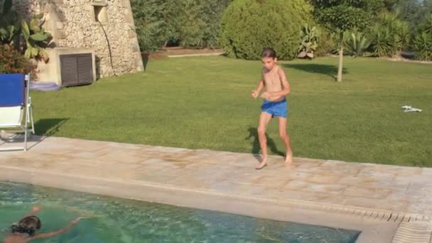 Preteen boy jumps into an outdoor pool, swims. Water play, summertime. — ストック動画