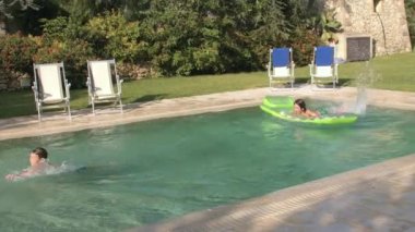 Kids uses inflatable mattress, swimming in pool. Boys enjoy active play in water