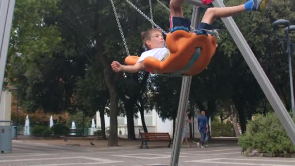 Boy play in the urban playground, swing on a swing. Kids-friendly space. — Wideo stockowe