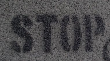  Stop word is stenciled with black paint on a gray wall surface. Protest sign