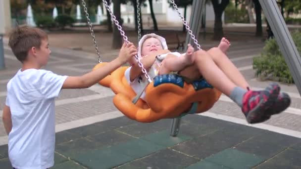 Children play in the city playground, swing on a swing. Kids-friendly space. — Vídeos de Stock