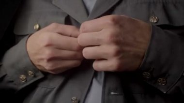 Close-up of hands fastening buttons on a gray uniform. The distinctive clothing.
