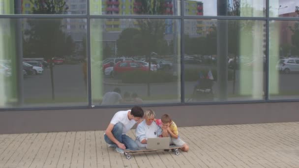 Skupina teenagerů používá notebook na skateboardu u skleněné stěny. — Stock video