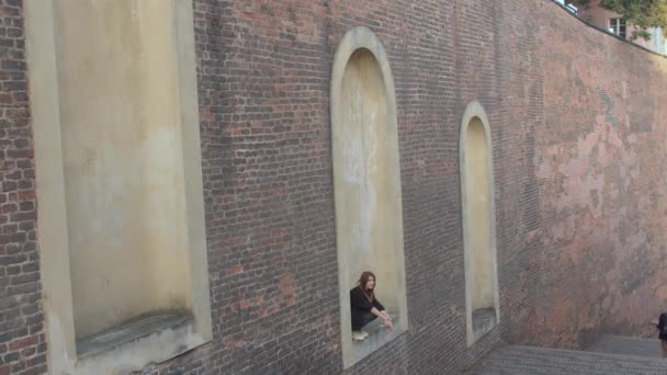 Девушка сидит в каменной нише старой городской стены. Свободное время от скуки. — стоковое видео