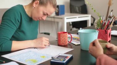 Kadın el boyası kağıdı maviye boyuyor. Psikoterapi gören hastaları çiziyor.
