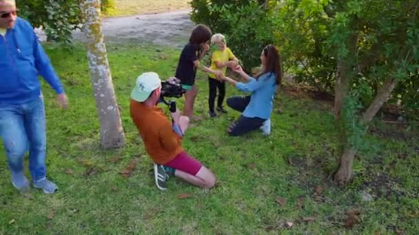 Мужчина с камерой записывает видео, мама приглашает детей попробовать сочные фрукты. — стоковое видео