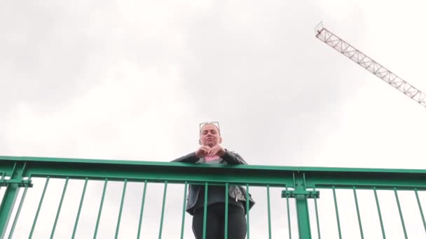 女性が橋の上に立ち、手すりの上に手を置いている。彼女は見下ろす. — ストック動画