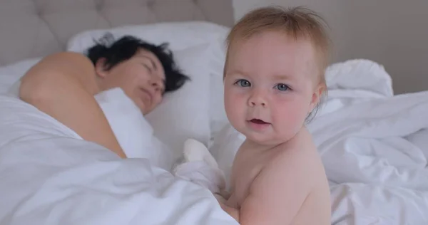 Bebê bonito posando com a mãe dormindo em uma cama branca. Compartilhar um sonho com uma criança — Fotografia de Stock