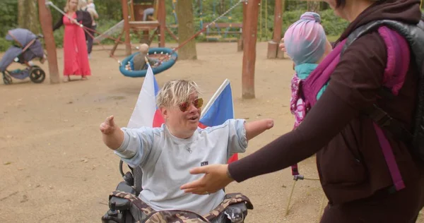 Mulher em cadeira de rodas cumprimenta seus amigos no parque infantil. Pessoas com necessidades especiais. — Fotografia de Stock