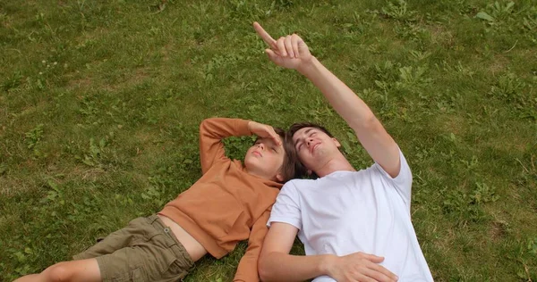 Chłopiec i młody mężczyzna leżą na trawie, patrząc w niebo. Widok z góry. — Zdjęcie stockowe