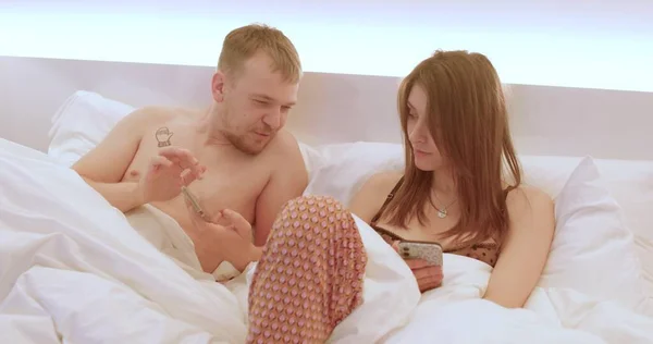 Un cuplu în pat se uită la ecranele telefoanelor. Petreceți timp pe rețelele sociale — Fotografie, imagine de stoc