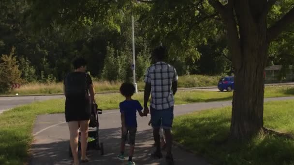 Rodzina spaceruje po chodniku w mieście. Cień drzewa, światło słoneczne. — Wideo stockowe