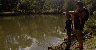Anne ve yeni doğmuş bir bebek taşıyıcısı ile çocuk şehir göletinde suyla oynuyor.