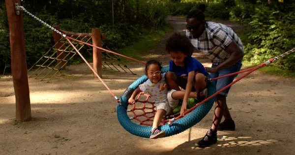 Father with children plays on playground, helps them train vestibular system. — Stockfoto