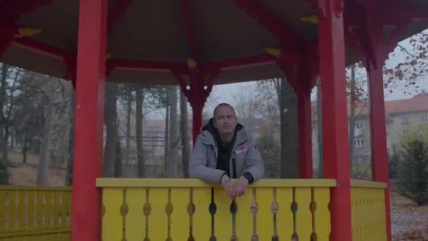 Un uomo si trova in un gazebo di legno. Sta aspettando di incontrarsi. Mani piegate. — Video Stock