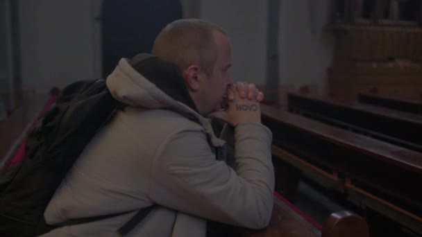 Muž se modlí, když sedí na lavičce v kostele. Drží se za ruce a hlavu. — Stock video
