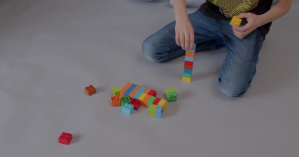 Niño jugando con juguete de construcción sobre un fondo gris. Forma de identidad de ladrillos. — Vídeo de stock