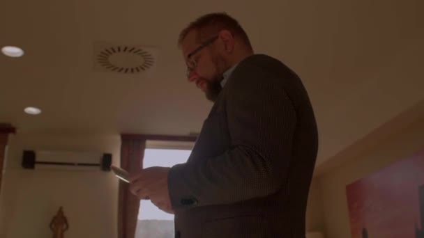 Бородатий чоловік використовує телефон в руках. Він дивиться на екран, натискає кнопки — стокове відео