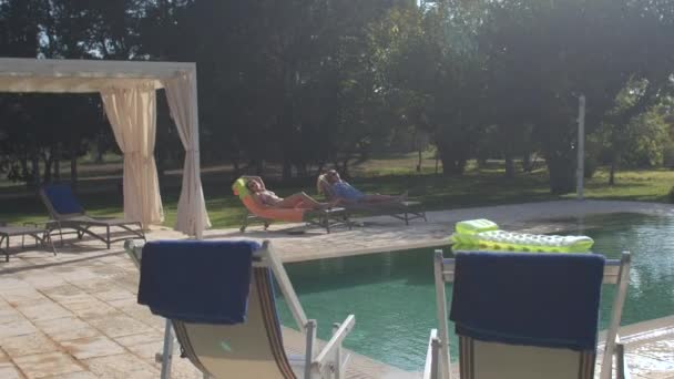 Cuerpo de relajación. Actividades de ocio vacaciones. Dos mujeres toman el sol en la piscina al aire libre. — Vídeos de Stock