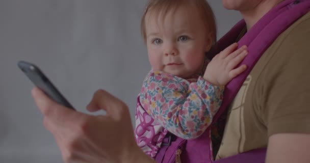 Skup się na telefonie w dłoniach ojciec dziecko siedzi w temblaku. — Wideo stockowe