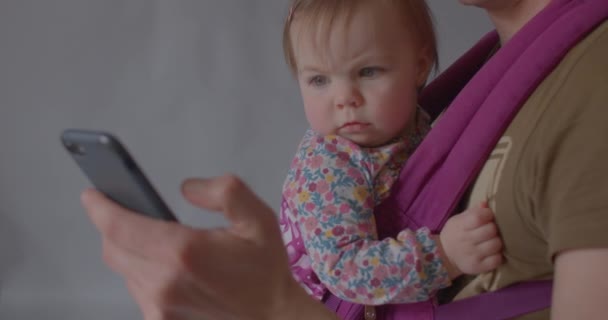 Schattige baby kijkt naar de telefoon met gefronste wenkbrauwen. Gezichtsuitdrukkingen van het kind — Stockvideo