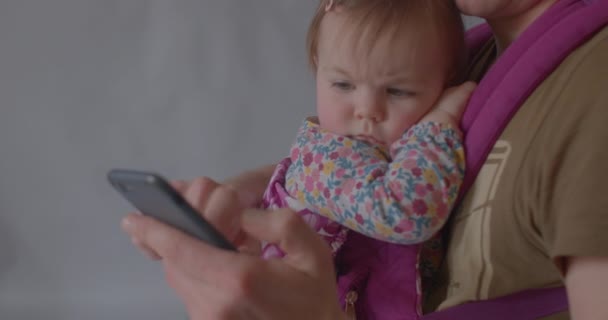 Nettes Baby blickt mit gerunzelten Augenbrauen auf das Telefon. Gesichtsausdruck des Kindes — Stockvideo