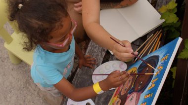 Palet, tuval ve boya fırçasıyla yetenekli bir çocuk resmi tamamlar..