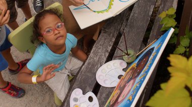 Palet, tuval ve boya fırçasıyla yetenekli bir çocuk resmi tamamlar..