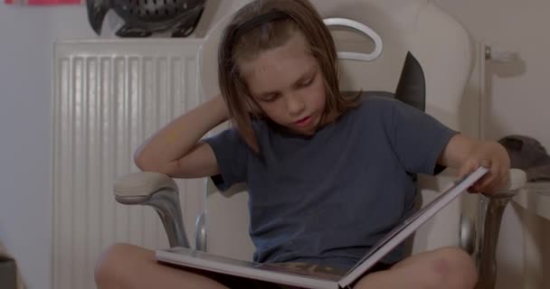 L'enfant feuillette, examine et lit un livre à la maison. Enseignement à domicile, lecture. — Video