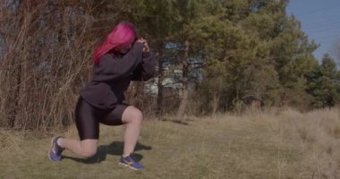 A red-haired woman makes lunges with her feet on the grass.
