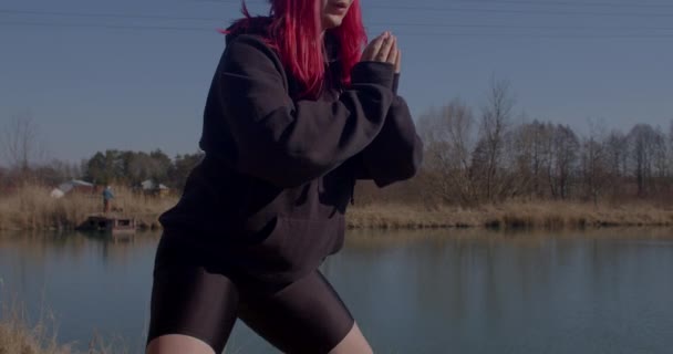 Redhead allenamento corpo donna sul fiume. Si tiene per mano davanti, piegando le ginocchia — Video Stock