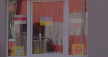 Çocuklar pencereye bayraklar asarlar. Ortada Ukrayna bayrağı var..