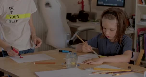 Empleo mesa de niño de pelo largo. Él pintando cuadro Hojas y lápices de mesa — Vídeo de stock