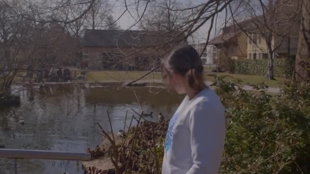 Meisje in de buurt van zonnige stedelijke vijver in het voorjaar. Gezondheidsvoordelen van stadspark wandelen — Stockvideo