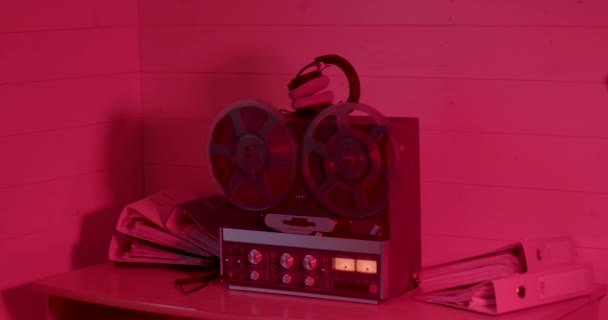 Sala de noche de luz roja Los carretes de cinta giran en una vieja grabadora. Dispositivo auriculares — Vídeos de Stock