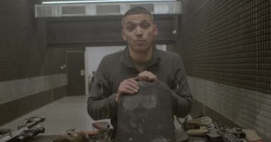 Adam medyaya yorum yapıyor, poligondaki kameraya bakıyor, çelik yeleği tutuyor.