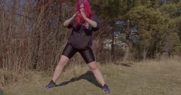 Frau mit roten Haaren beim Beintraining in der Sonne. Sie setzt sich auf ein Bein. — Stockvideo