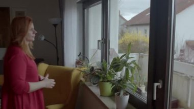 Pencerenin yanında kırmızı elbiseli düşünceli genç bir kadın var. Emekliliği ifade etmek.