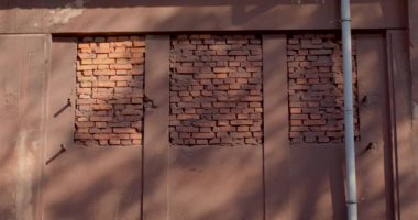 Burgonya rengi, endüstriyel bir binanın beton duvarı. Pencere açılması tuğlalarla kaplı. Beyaz yağmur borusu. Ağaçların gölgesi.