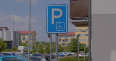 Mavi arka planda engelli işareti beyaz, uluslararası park yeri tanımlaması. Trafiğin arka planına karşı. Şehir merkezinde güneşli bir gün.