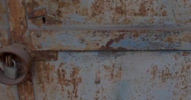 Çizik içinde paslı eski bir kapı. Kapıda metal çerçeveli eski bir kilit asılı. Giriş yasağı, eski evin kapısını kilitlemiş. Metal paslanma.