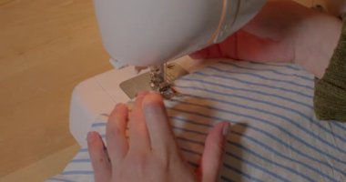 Yakın plan. Dikiş makinesine dikiş dikmiş bir terzinin elleri. Kumaşı ve iğnenin hareketini yerleştiriyor ve bir çizgi oluşturuyor. Cezaevinde çalış, tutukla.